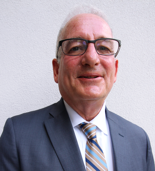 Photo of Jay Beskin, an elderly man with glasses smiling slightly, wearing a gray suit and striped tie. He is against a plain white wall, conveying professionalism.