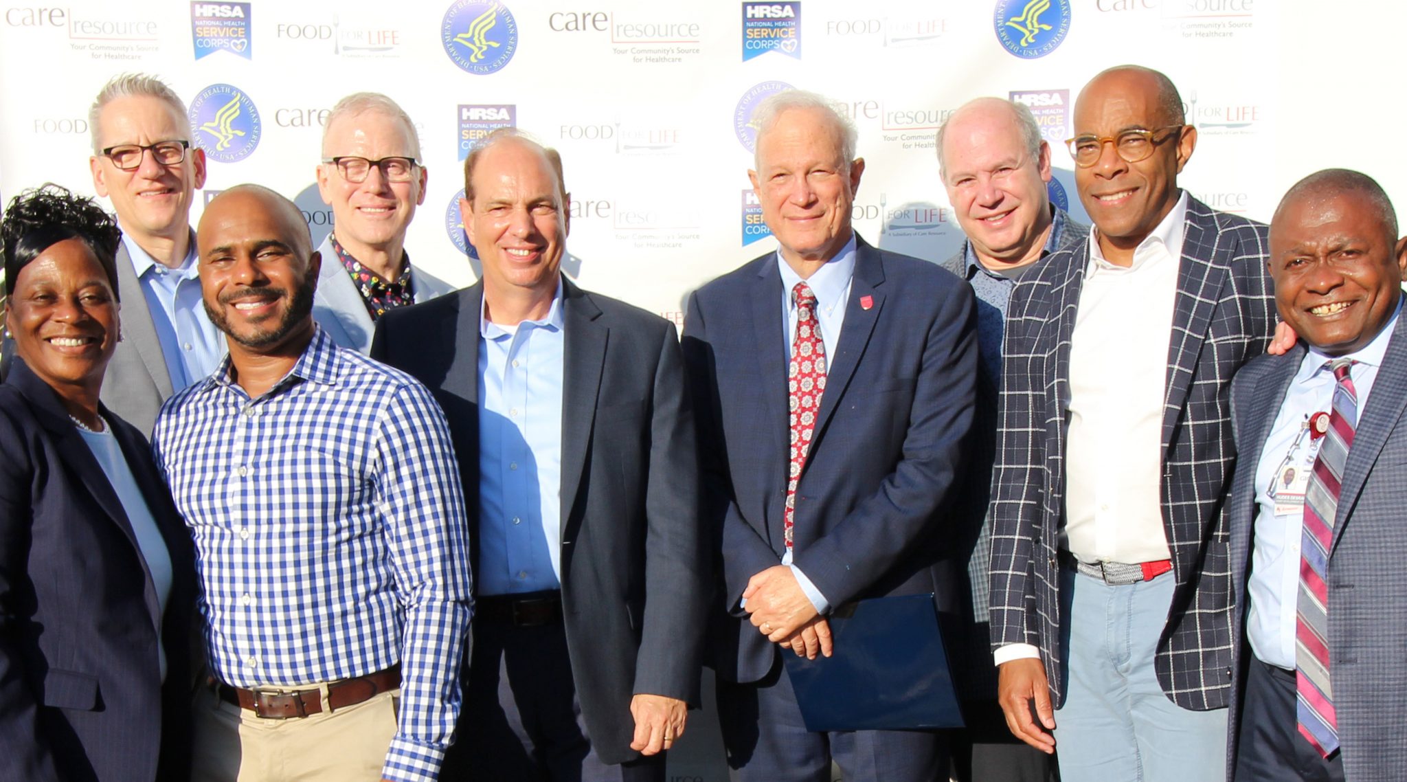 Members of the Presidential Advisory Council on HIV/AIDS (PACHA) and federal partners pose for a photo in front of a step and repeat wall of logos.