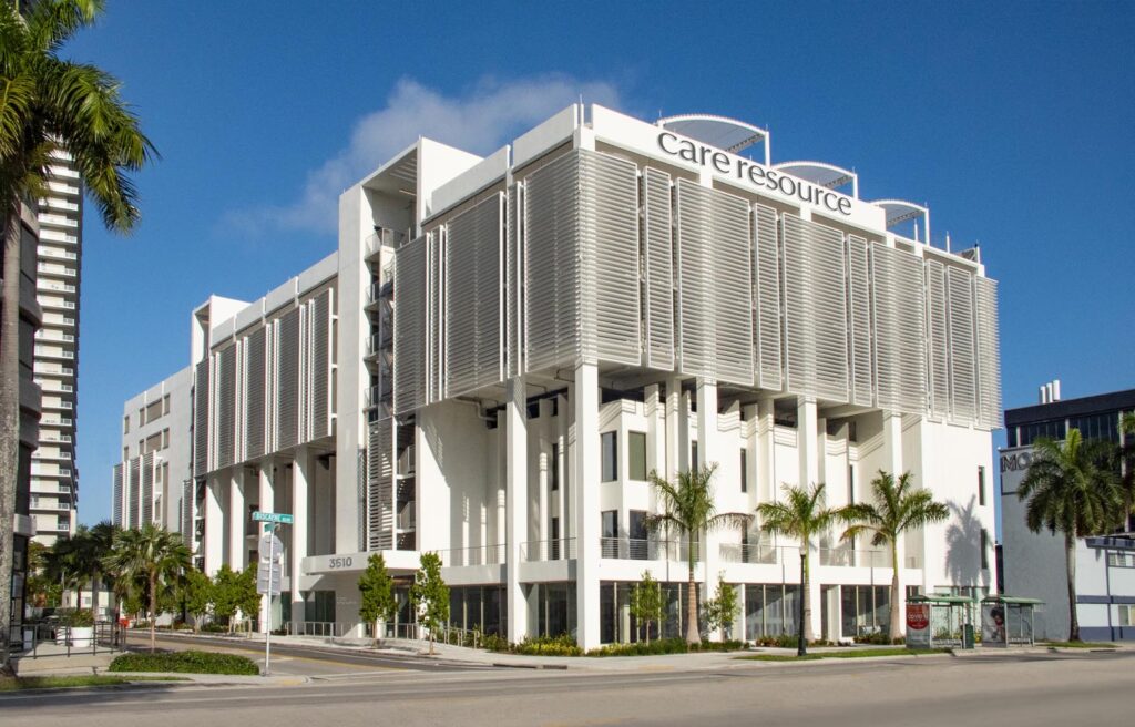 Modern building with sleek architecture and palm trees, labeled Care Resource. Bright and sunny atmosphere with a clear blue sky.