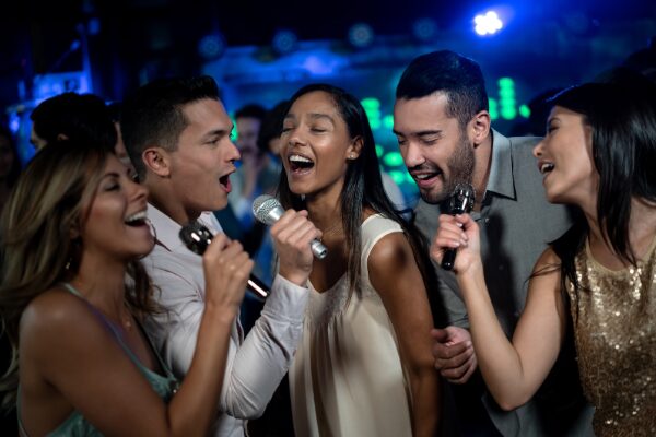 Conveying awareness of High-Intensity Drinking, a photo of a group of five people joyfully singing into microphones at a lively karaoke event. They seem animated and happy, with colorful lights in the background.