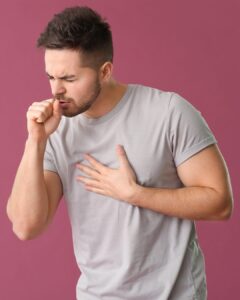 Someone wearing a grey t-shirt and coughing