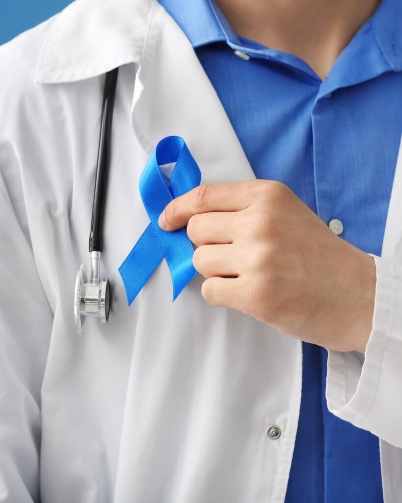 a person wearing a white lab coat, over a blue shirt, holding a blue ribbon.