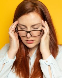 Woman with glasses, holding the sides of her face.