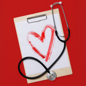 A stethoscope rests on a clipboard with a red heart painted on paper against a red background, symbolizing heart health and medical care for American Heart Month.