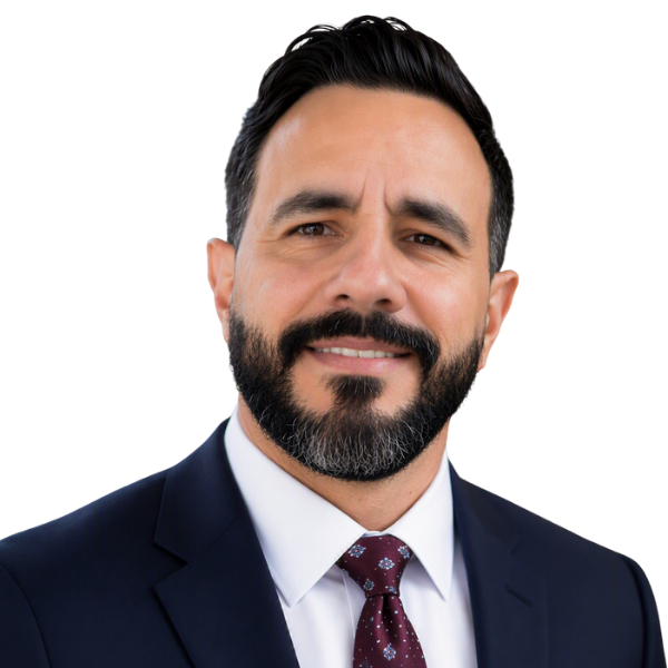 A photo of Manuel Casas, DMD, a man with short dark hair and a beard in a navy suit, white shirt, and maroon tie.