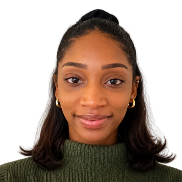 Portrait of Arielle Bowleg. a smiling woman with a top bun, shoulder-length hair, gold hoop earrings, and a dark green sweater on a white background.
