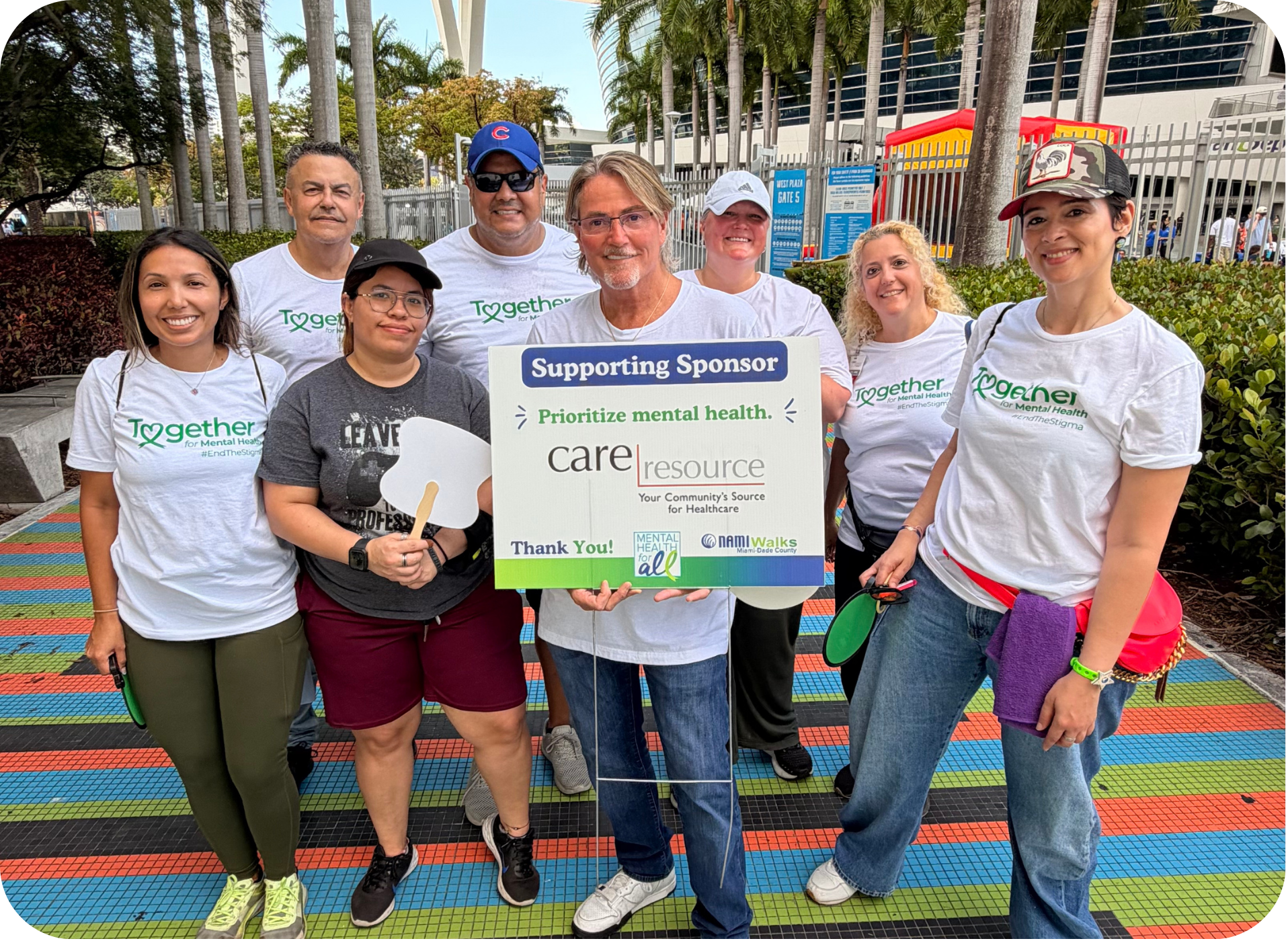 Seven volunteers in Together-branded shirts pose outdoors, holding a “Supporting Sponsor” sign promoting mental health care at a community event.