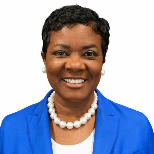 A photo of a smiling woman with short hair, pearl necklace, white top, and bright blue blazer against a white background.
