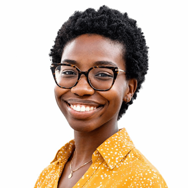 Smiling photo of Khloey Jean-Baptiste, a woman with short natural hair and round glasses wears a mustard-yellow polka-dot shirt, projecting warmth and confidence.
